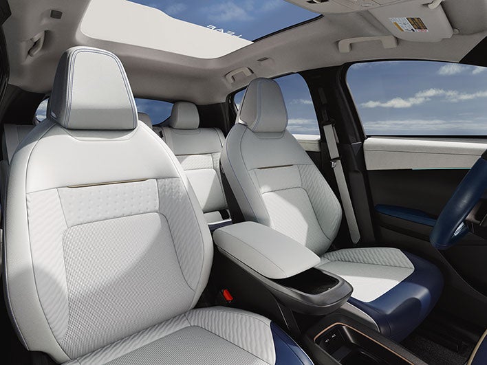 The interior of a car with light gray seats, a panoramic sunroof, and a blue dashboard accent.